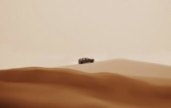 Wallpaper A Car Driving Through the Desert Under a Full Moon