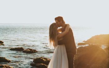 Wallpaper Man and Woman Kissing on Top of Gray Rock at Beach