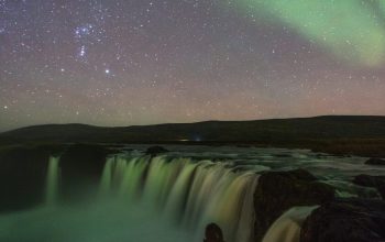Wallpaper Person Sitting Near Waterfalls Under Aurora Lights