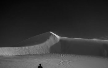 Wallpaper A Man Walking Across a Sandy Desert Under a Dark Sky