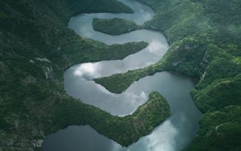 Wallpaper A River Flowing Through a Lush Green Valley