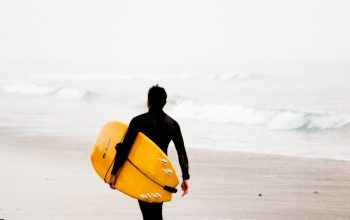 Wallpaper Man Holding Yellow Surfboard on Seashore