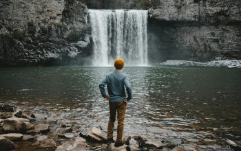 Wallpaper Man Standing on Brown Stone Facing Waterfalls