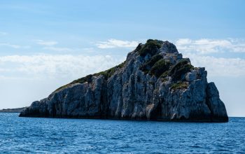 Wallpaper Brown and Green Rock Formation on Sea Under Blue Sky