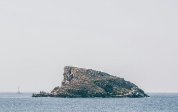 Wallpaper Brown and Green Rock Formation on Sea Under White Sky