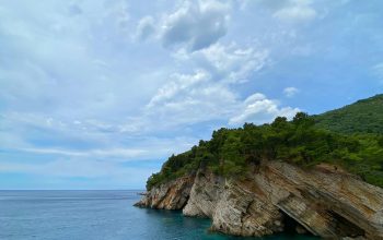 Wallpaper Green and Brown Mountain Beside Blue Sea Under White Clouds and Blue Sky
