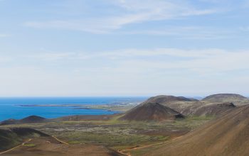 Wallpaper Brown and Green Mountain Beside Sea Under Blue Sky