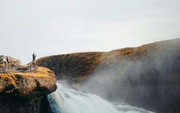 Wallpaper Two People Standing on a Cliff Above a Waterfall