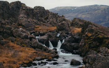 Wallpaper A Stream Running Through a Rocky Landscape with a Mountain in the Background