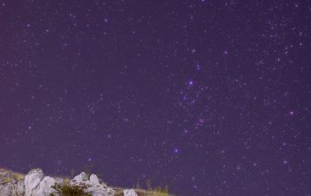 Wallpaper The Night Sky is Filled with Stars Above a Rocky Hill