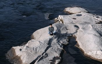 Wallpaper A Person Sitting on a Rock in the Middle of a River