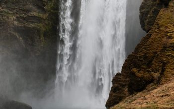 Wallpaper A Large Waterfall with a Man Standing in Front of It