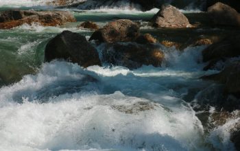 Wallpaper A Man Standing on Top of a Rock Next to a River