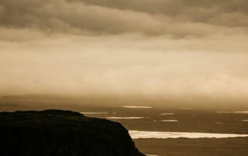 Wallpaper A Person Standing on Top of a Hill Under a Cloudy Sky