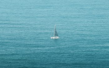 Wallpaper A Lone Sailboat in the Middle of the Ocean