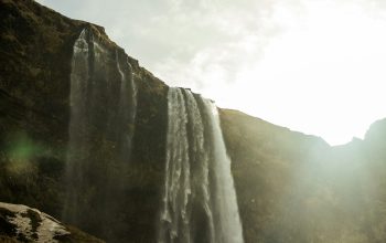 Wallpaper A Large Waterfall with a Man Standing on Top