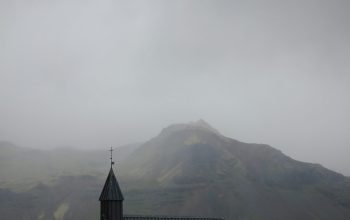 Wallpaper A Small Black Church with a Steeple on a Cloudy Day
