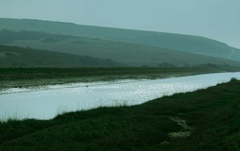 Wallpaper A Serene River Flows Through Lush Green Landscape