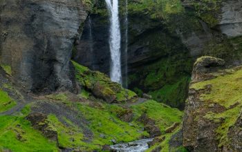 Wallpaper A Waterfall Cascades Down a Lush Green Canyon