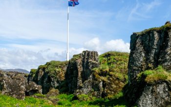 Wallpaper Icelandic Flag Waves Above a Rocky, Floral Landscape